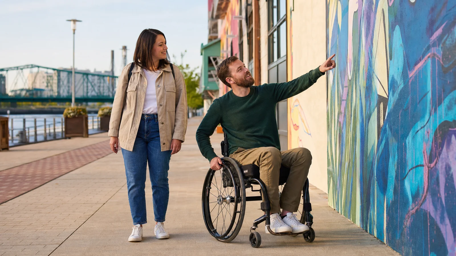 A couple talking beside a riverside mural, with one partner using a manual wheelchair