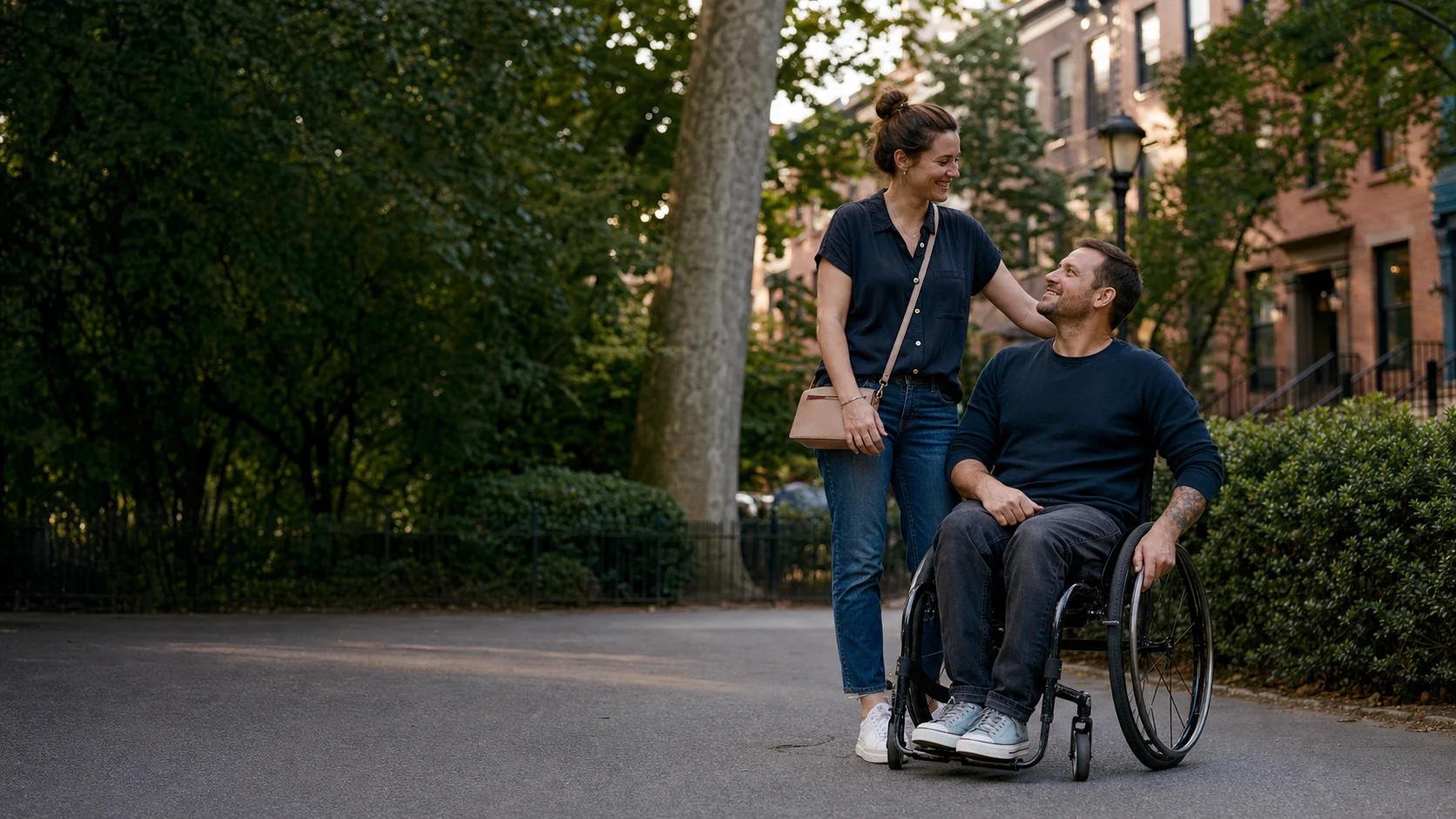 A white American couple sharing a relaxed moment in a neighborhood park, with one partner using a wheelchair